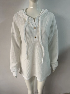 Détail de la texture gaufrée blanche et boutons en bois sur le pull à capuche