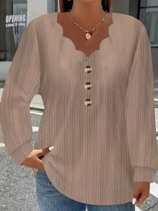 Close-up of scallop V-neckline with decorative buttons on textured beige long sleeve top