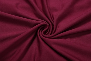 Close-up of deep red knit fabric showing soft texture and elegant draped silk-like finish