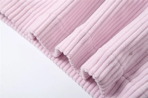 Detail of pink corduroy fabric showing soft vertical ribbed texture and hem stitching
