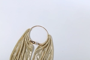 Dettaglio del tessuto metallico dorato con anelli lucidi su un top con scollo a barchetta