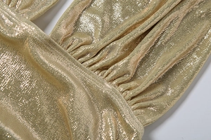 Dettaglio macro del tessuto metallico dorato con pieghe sottili e cuciture incrociate nette