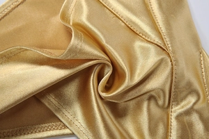 Gros plan sur un tissu doré champagne brillant avec haute élasticité et coutures doubles