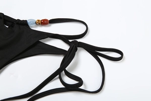 Detail of black bikini side tie featuring three colorful decorative beads on white background