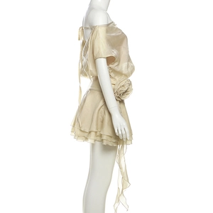 Détail de robe champagne à épaules dénudées avec fleur géante et jupe plissée élégante