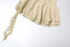 Détail de la robe courte en mousseline beige avec volants superposés et longs lacets