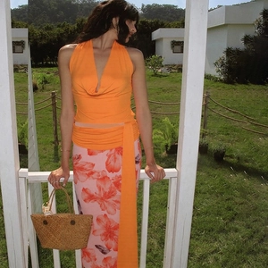 Detail of a bright orange halter top with long waist ties and vibrant floral maxi skirt