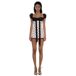 Detail of white polka dot mini dress featuring black lace trim and a large bow tie