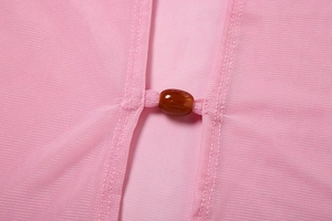 Macro detail of pink mesh fabric featuring a translucent amber resin bead button closure