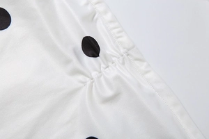 Close-up of white silky fabric with large black polka dots and pleated detail craftsmanship
