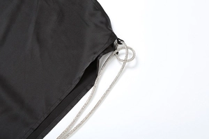 Detail of high side slit on black satin skirt featuring sparkling rhinestone ties and rings