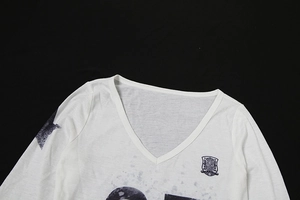 Detail eines weißen Langarm-T-Shirts mit V-Ausschnitt, schwarzem Wappen und Buchstabendruck