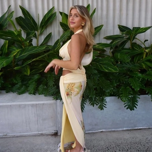 Detail of a backless halter top and side-slit floral maxi skirt in soft yellow fabric