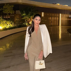 Detail of khaki deep V-neck pleated jumpsuit paired with a white structured blazer
