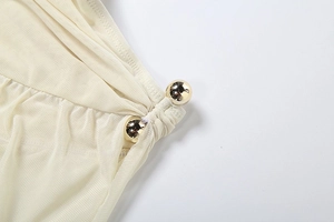 Detail of off-white mesh fabric with golden spherical metal hardware on a halter top