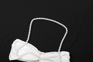 Detail aus weißem Plissee-Stoff mit eleganten Perlenketten-Trägern an einem Top