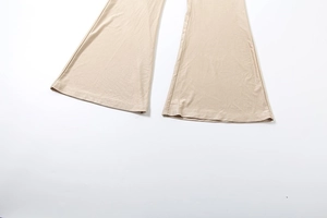 Detail shot of apricot flared trousers featuring wide leg openings and smooth knitted fabric