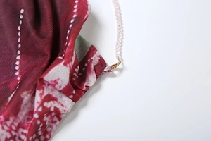 Détail de bretelles en perles roses avec fermoirs dorés sur une robe à fleurs rouges