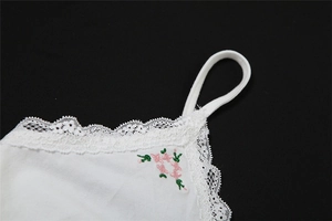 Détail de caraco blanc avec bordure en dentelle délicate et broderie florale rose