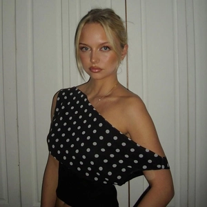 Detail of the black one-shoulder top with white polka dots and asymmetric neckline