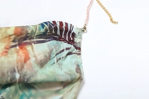 Détail de perles roses et chaînes dorées sur une robe dos nu à imprimé floral coloré