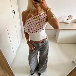 Detail of white red polka dot one shoulder crop top with high waist denim jeans and gold jewelry