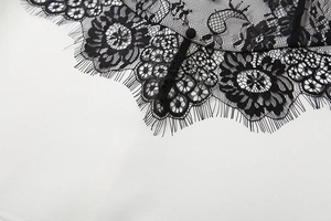 Détail de dentelle florale noire délicate avec bordure cils et bouton en tissu sur robe