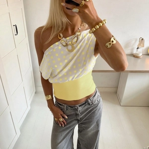Detail of one-shoulder polka dot crop top paired with yellow belt and layered gold necklaces