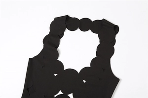 Detailed close-up of laser-cut geometric patterns and wave-edge neckline on black fabric