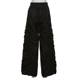 Detail of black parachute pants with pleated design and nylon textured fabric finish