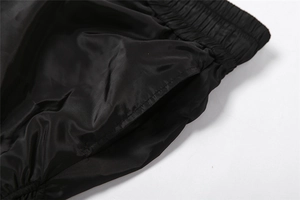 Detail view of the elastic pleated waistband and side pocket stitching on black trousers