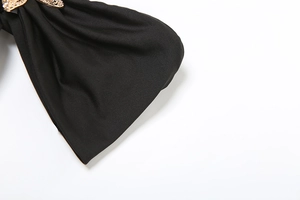 Detail of a large black textured fabric bow featuring a vintage gold embossed buckle accent