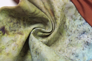 Macro shot of rib-knit fabric with tie-dye patterns in olive, ochre, and blue tones