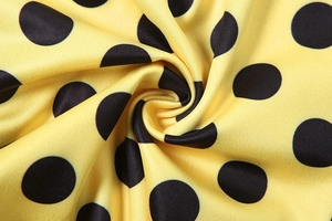 Dettaglio macro del tessuto giallo con pois neri e morbide pieghe a spirale elastiche
