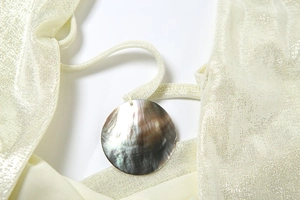Détail macro du tricot scintillant et du pendentif circulaire en nacre sur le haut