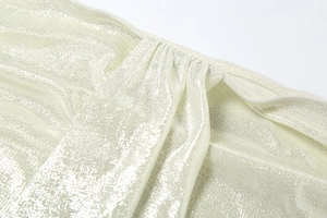 Gros plan sur un tissu métallisé or champagne avec texture horizontale et détails plissés