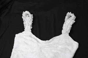 Détail du haut en dentelle blanche avec bretelles à volants et nœud torsadé sur soie noire