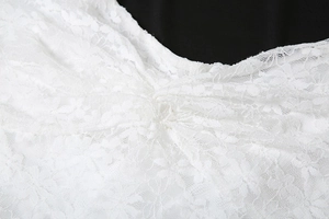 Détail de dentelle blanche crochetée avec motifs floraux et plis sur la robe ajustée