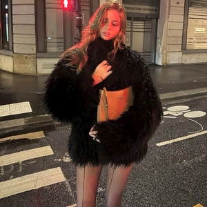 Close-up of black fluffy faux fur jacket texture with a glossy shoulder bag