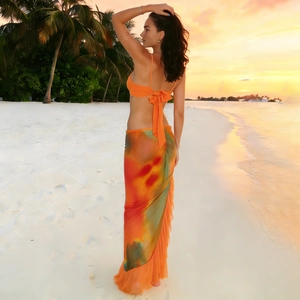 Detailed view of vibrant tie-dye ruffled skirt and orange bikini top on a sunset beach