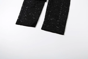 Détail de pantalon noir en dentelle florale avec motifs ajourés et texture transparente
