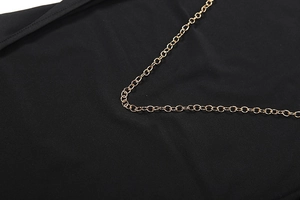 Detail of gold chain decoration on backless black dress with premium fabric texture