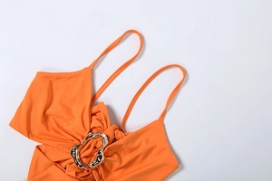 Close-up of bright orange halter top with elegant golden metal ring and thin straps