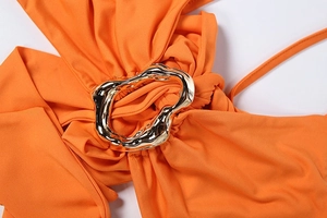 Close-up of bright orange draped fabric with a molten-effect gold metal buckle detail