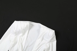 Détail de la robe blanche à col en V profond montrant les plis d'épaule et le tissu lisse