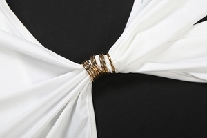 Détail du tissu blanc de la robe avec des anneaux dorés créant un design plissé chic