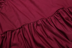 Gros plan sur un tissu texturé bordeaux avec fronces détaillées et coutures précises