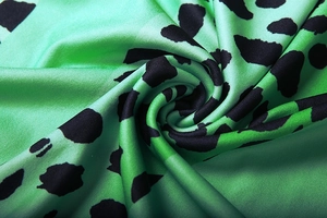Macro detail of silky green satin fabric with black animal print texture and sheen