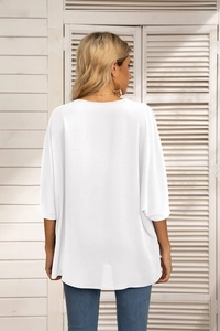 Back view of a white chiffon blouse with batwing sleeves and a curved hem on a model