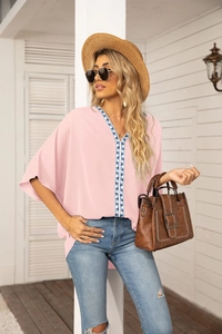 Detail of pink chiffon blouse with ornate blue geometric embroidery and batwing sleeves